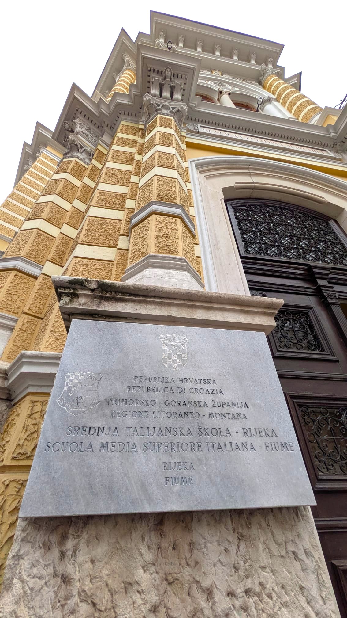 Insegna in pietra della Scuola Media Superiore Italiana a Fiume, evidenziando il nome e la posizione dell'istituto scolastico.