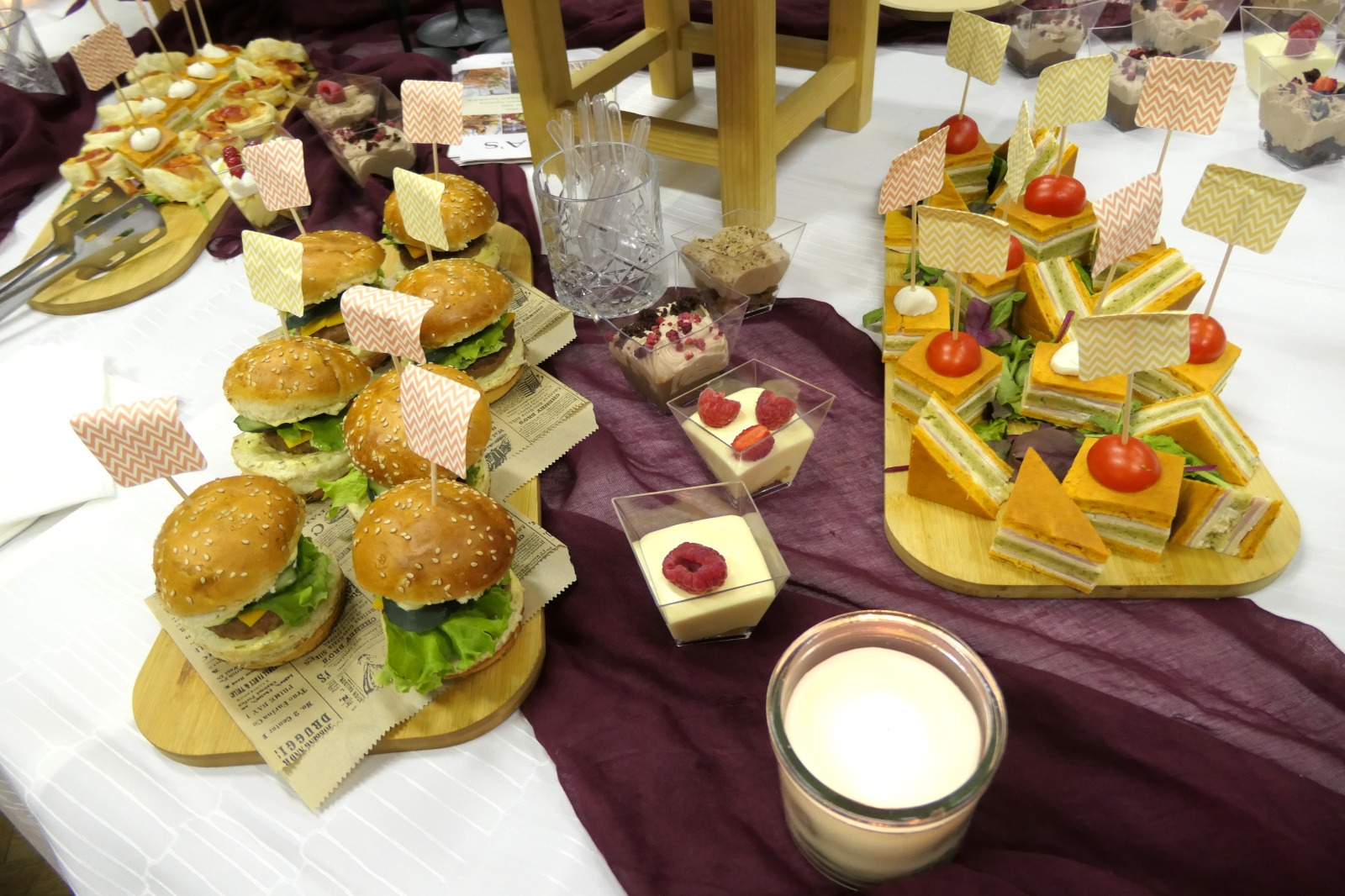 Piatto di antipasti con hamburger mini di sesamo e tramezzini colorati decorati con bandierine e pomodorini, serviti su un tavolo decorato.