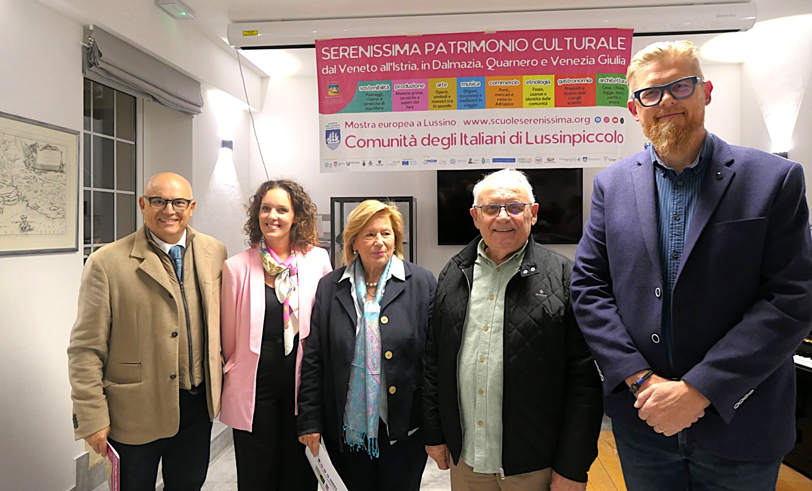 Gruppo di persone in un evento culturale, davanti a un banner che promuove il patrimonio culturale della Serenissima.
