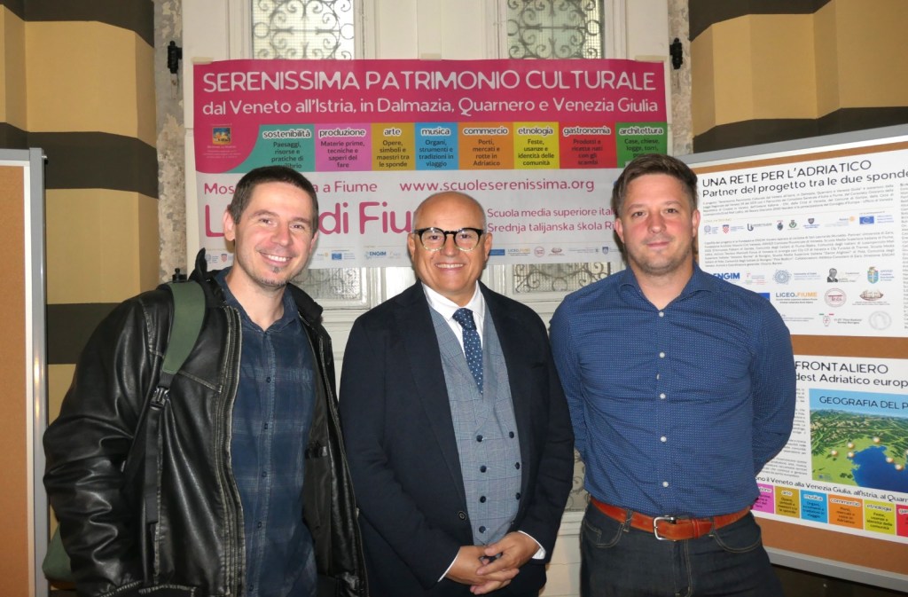 Tre uomini sorridenti in un evento legato al patrimonio culturale, davanti a un poster informativo sull'Adriatico e le sue tradizioni.